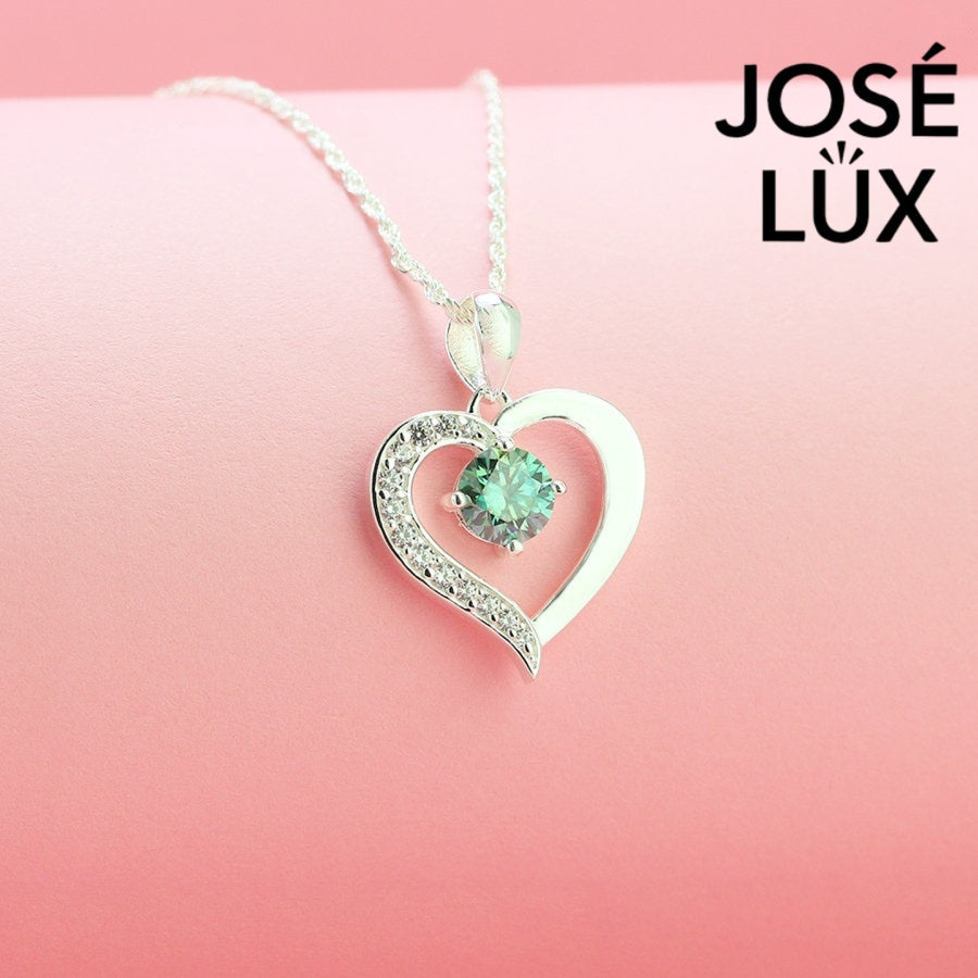 Enchanting 0.6ct round green moissanite open heart pendant features vibrant colored stone with pavé accents, romantically crafted in polished sterling silver.