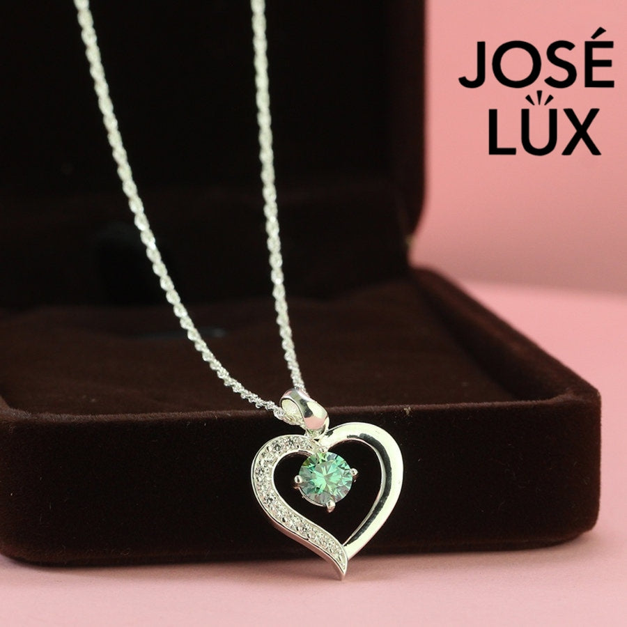 Enchanting 0.6ct round green moissanite open heart pendant features vibrant colored stone with pavé accents, romantically crafted in polished sterling silver.