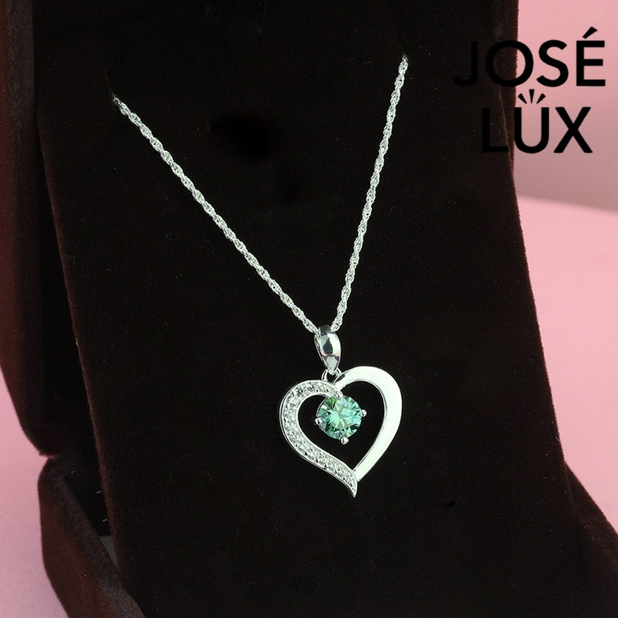 Enchanting 0.6ct round green moissanite open heart pendant features vibrant colored stone with pavé accents, romantically crafted in polished sterling silver.