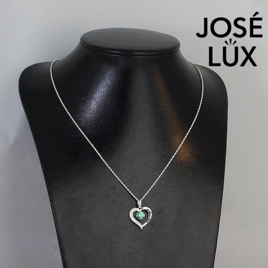 Enchanting 0.6ct round green moissanite open heart pendant features vibrant colored stone with pavé accents, romantically crafted in polished sterling silver.