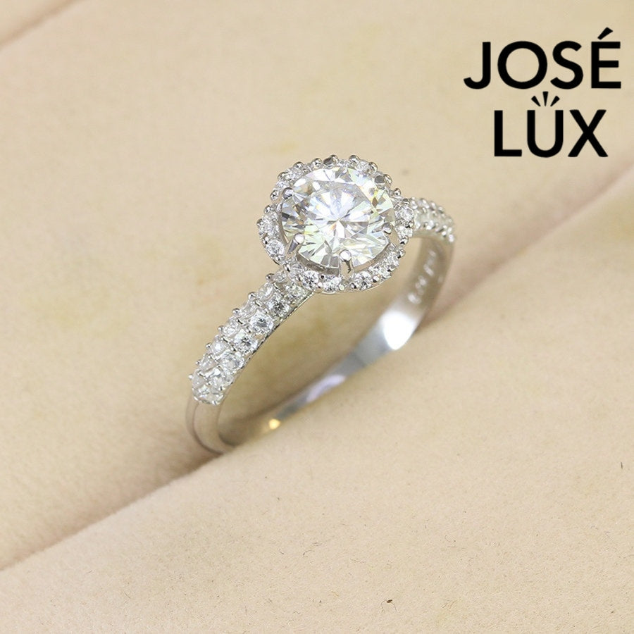 Classic halo design features brilliant moissanite centerpiece with shimmering accent stones creating timeless elegance on a refined silver setting.