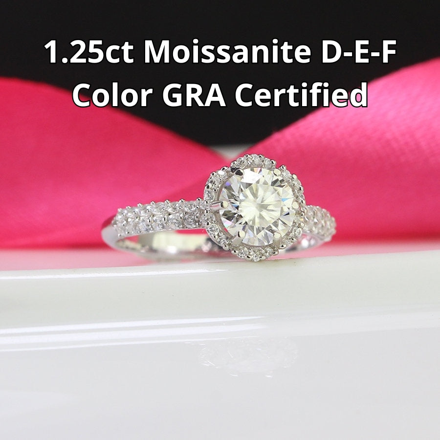 Classic halo design features brilliant moissanite centerpiece with shimmering accent stones creating timeless elegance on a refined silver setting.