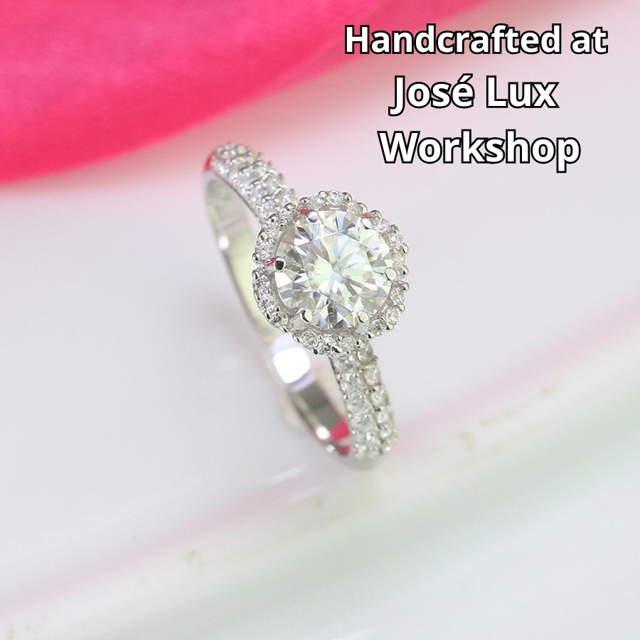 Classic halo design features brilliant moissanite centerpiece with shimmering accent stones creating timeless elegance on a refined silver setting.