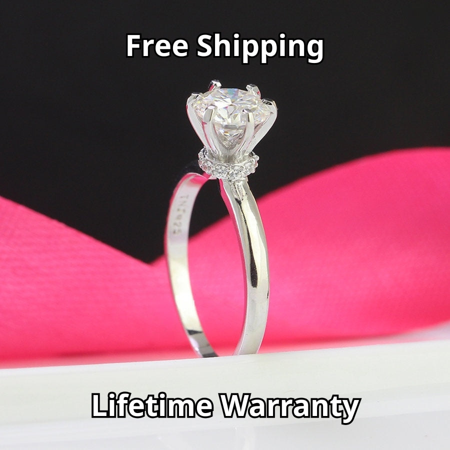 Traditional solitaire setting highlights brilliant round moissanite on a sleek silver band for timeless sophistication and everyday wearability.