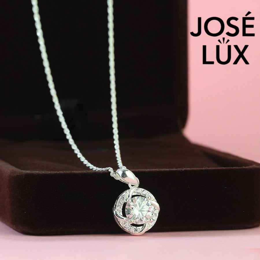 Intricate 1.2ct round moissanite twisted knot halo pendant showcases stunning center stone within pavé-accented interwoven design, artfully created in polished sterling silver.