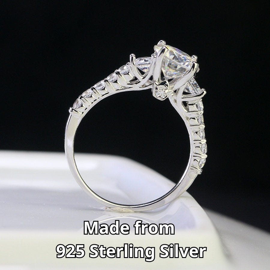 Brilliant 1.5ct moissanite center stone with sparkling side accents set in polished sterling silver creates timeless elegance for any occasion.