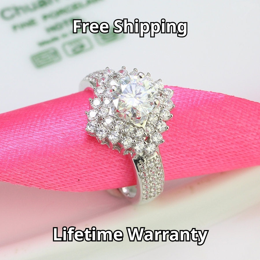 Brilliant round moissanite centerpiece enhanced by dual layers of sparkling accent stones with pavé detailing on the polished silver band.