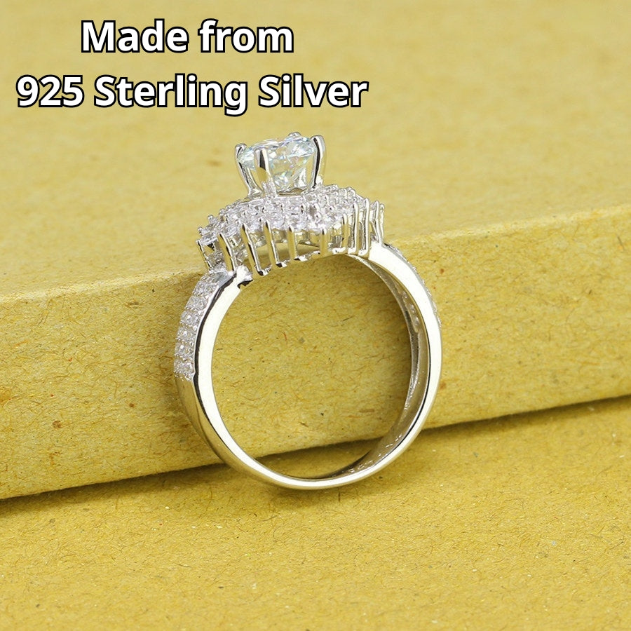 Brilliant round moissanite centerpiece enhanced by dual layers of sparkling accent stones with pavé detailing on the polished silver band.