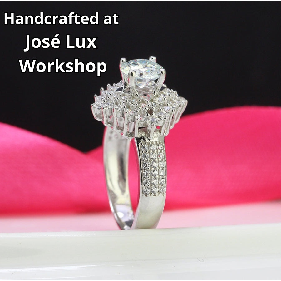 Brilliant round moissanite centerpiece enhanced by dual layers of sparkling accent stones with pavé detailing on the polished silver band.