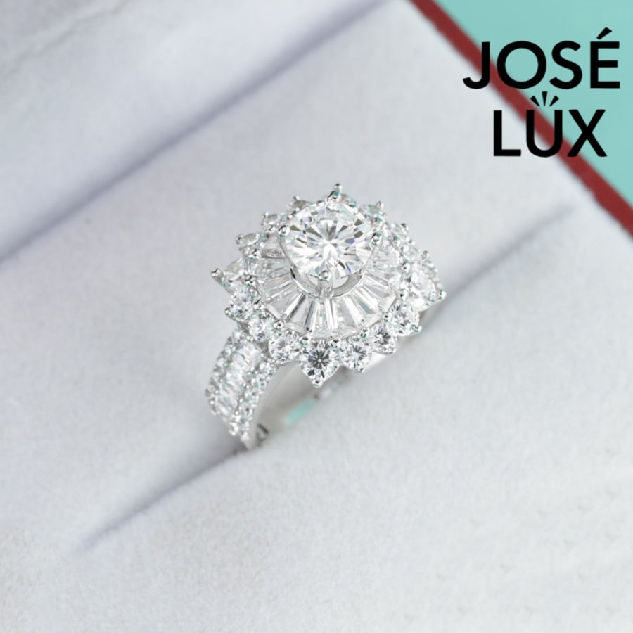 Stunning sunburst design features brilliant round moissanite surrounded by baguette and round accent stones with sparkling pavé band detailing.