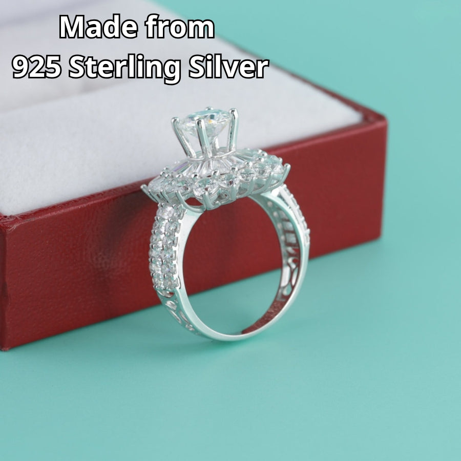 Stunning sunburst design features brilliant round moissanite surrounded by baguette and round accent stones with sparkling pavé band detailing.