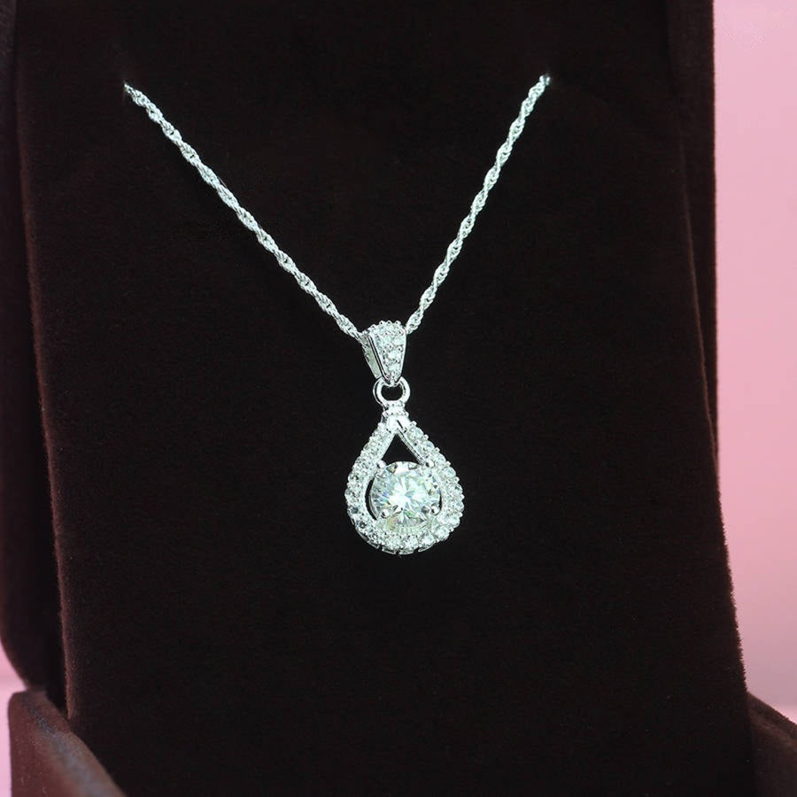 Contemporary 1ct round moissanite open teardrop halo pendant showcases brilliant center stone within elegant wishbone frame, beautifully designed in sterling silver.