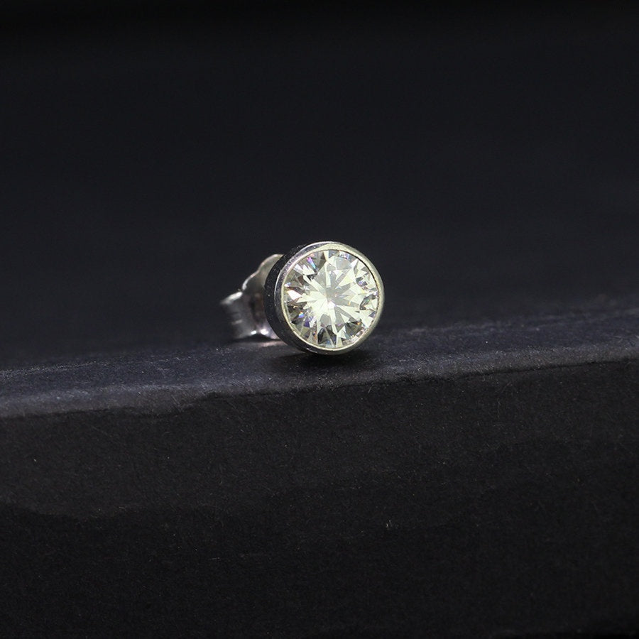 Close-up of 0.5ct moissanite stud in sterling silver bezel setting, highlighting brilliance and craftsmanship on dark surface.