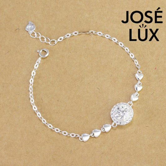 Cable chain halo moissanite bracelet in sterling silver features round brilliant centerpiece with heart accents weighing 1.0 carat on adjustable chain design.