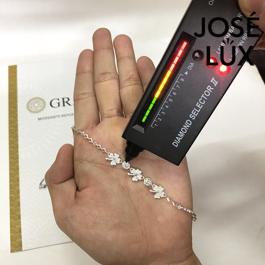 Four-leaf clover moissanite bracelet in sterling silver features three symbolic charms with two brilliant stones totaling 0.68 carats on geometric link chain.