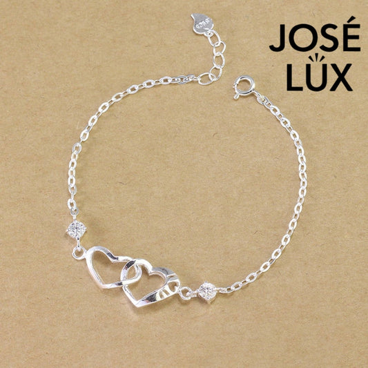 Interlocked hearts cable moissanite bracelet in sterling silver features romantic double heart centerpiece with two brilliant stones totaling 0.6 carats on adjustable chain.
