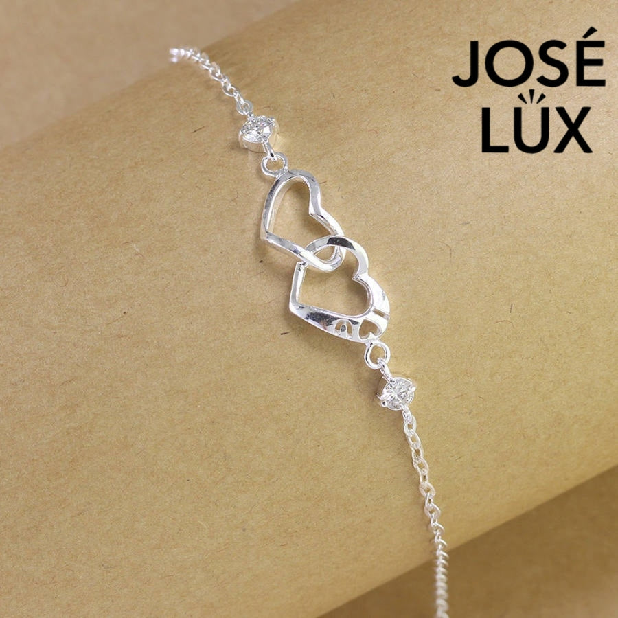 Interlocked hearts cable moissanite bracelet in sterling silver features romantic double heart centerpiece with two brilliant stones totaling 0.6 carats on adjustable chain.