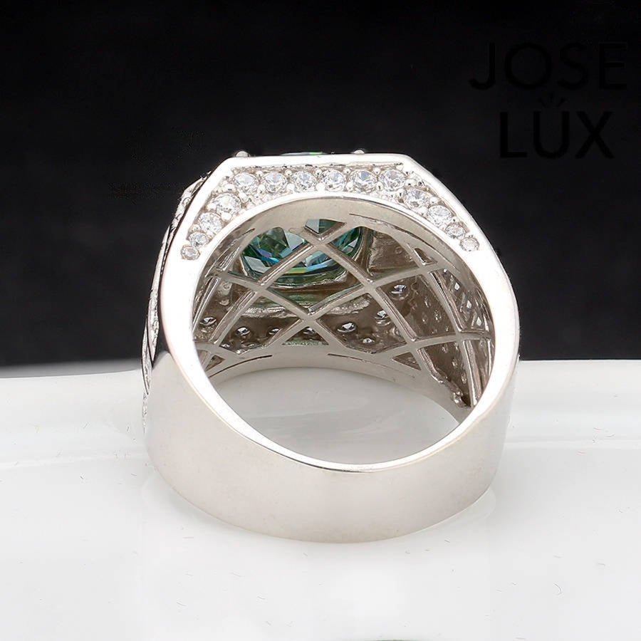 Substantial sterling silver men's ring featuring a 4-carat round green moissanite encircled by a cushion-shaped halo. Wide band with alternating rows of round and baguette stones creates impressive depth and dimension.