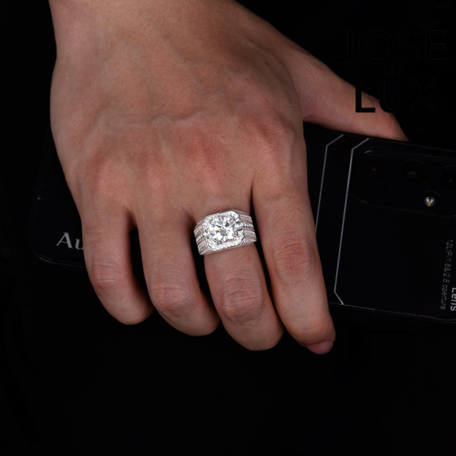 Striking men's ring in sterling silver showcases a brilliant 4-carat round moissanite within an octagonal double halo. Wide band features tiered baguette channels and pavé rows for exceptional sparkle and dimensional design.