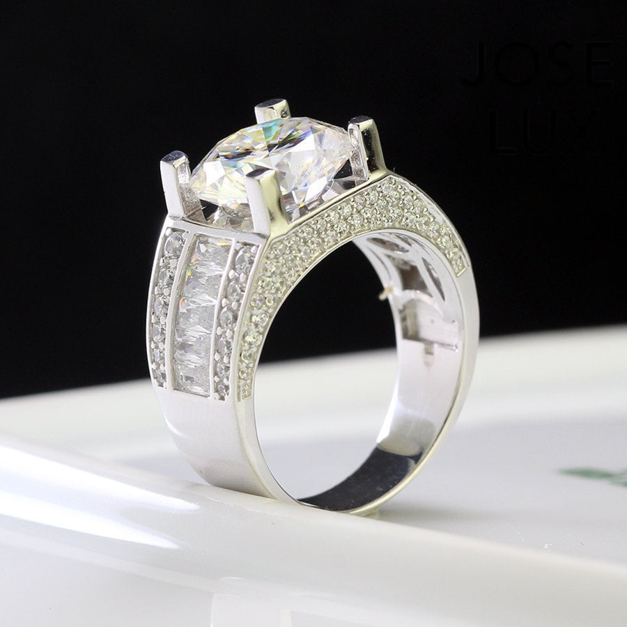 Classic men's ring in sterling silver showcases a brilliant 4-carat round moissanite in four-prong setting. Wide triple-row band features vertical baguette channels bordered by pavé stones for timeless sophistication.