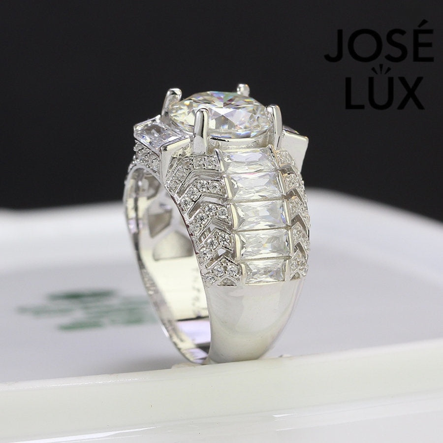 Commanding men's ring in sterling silver features a brilliant 4-carat round moissanite in six-prong setting. Wide band showcases graduated baguette-cut stones in chevron pattern with pavé accents for dimensional impact.