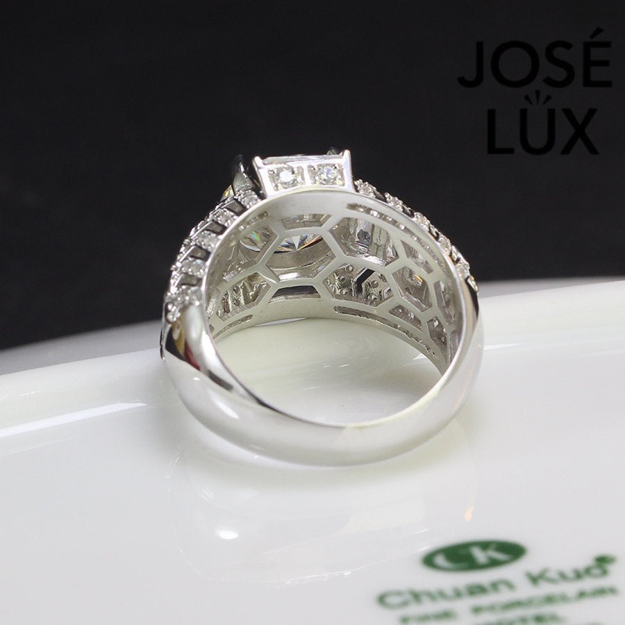 Commanding men's ring in sterling silver features a brilliant 4-carat round moissanite in six-prong setting. Wide band showcases graduated baguette-cut stones in chevron pattern with pavé accents for dimensional impact.