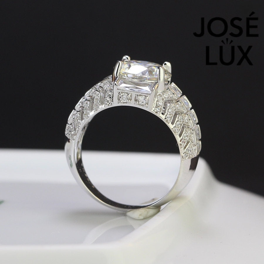 Commanding men's ring in sterling silver features a brilliant 4-carat round moissanite in six-prong setting. Wide band showcases graduated baguette-cut stones in chevron pattern with pavé accents for dimensional impact.