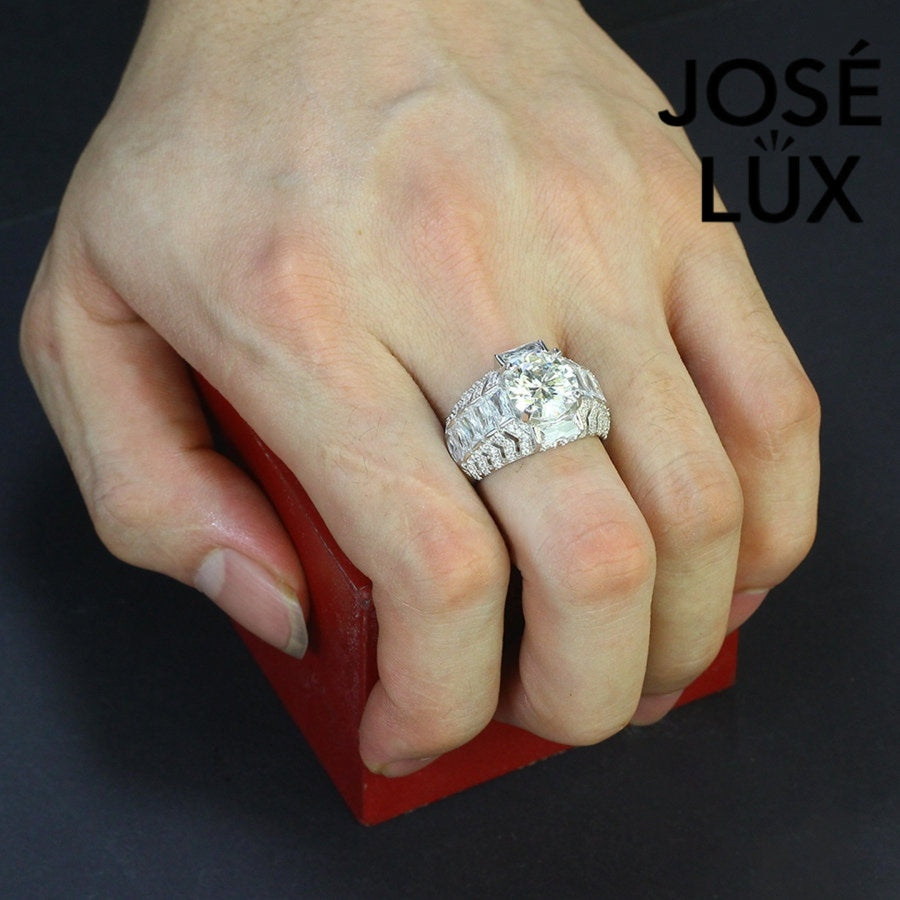 Commanding men's ring in sterling silver features a brilliant 4-carat round moissanite in six-prong setting. Wide band showcases graduated baguette-cut stones in chevron pattern with pavé accents for dimensional impact.