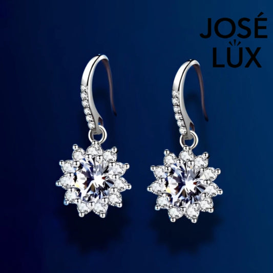 Delicate snowflake-inspired moissanite earrings with sparkling halo setting in sterling silver. Graceful dangle design adds elegant movement and brilliant fire to complement any style.