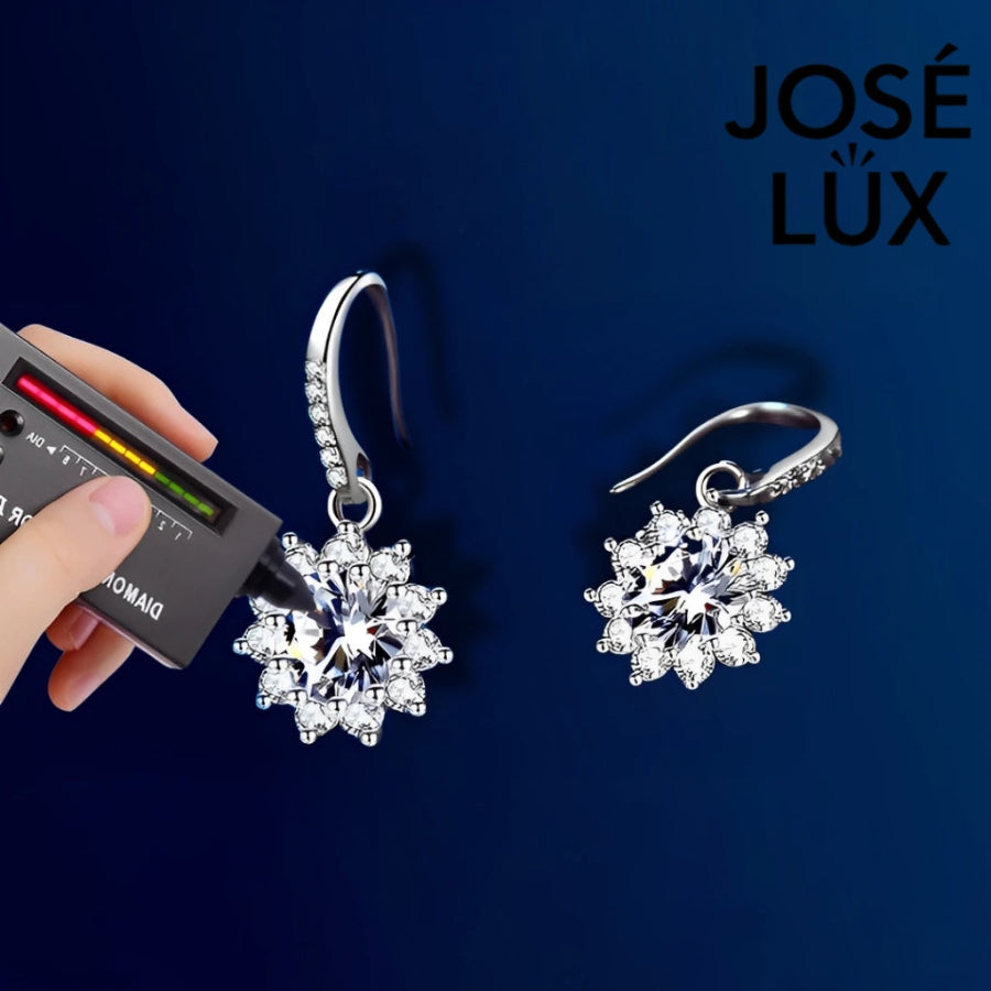 Delicate snowflake-inspired moissanite earrings with sparkling halo setting in sterling silver. Graceful dangle design adds elegant movement and brilliant fire to complement any style.