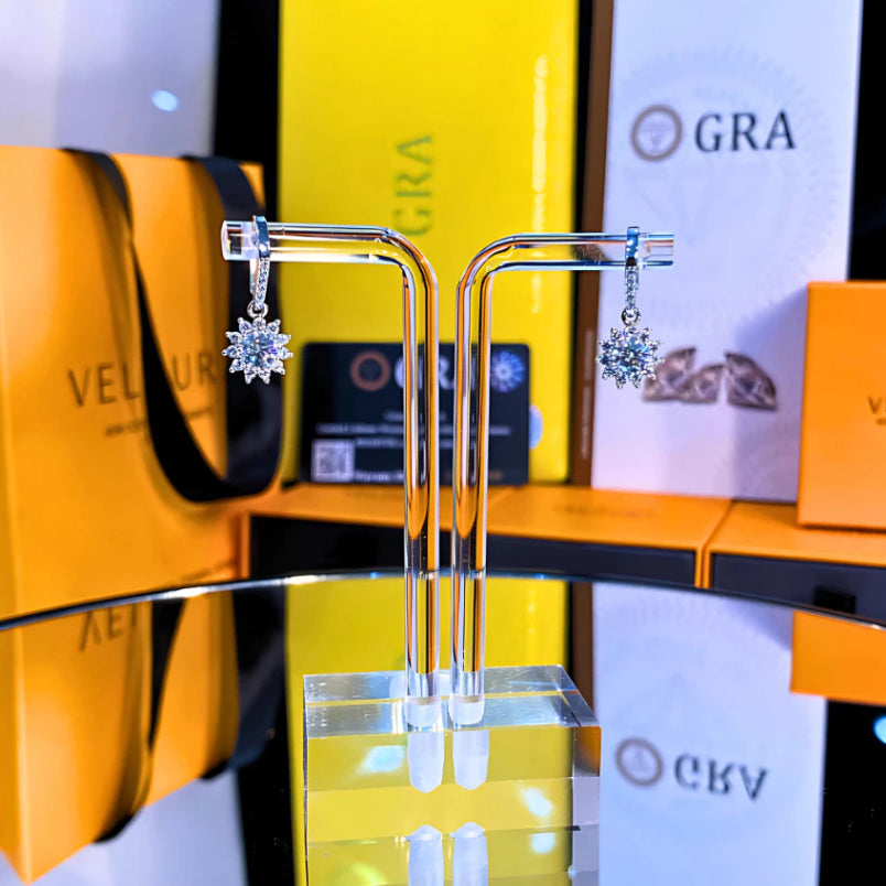 Delicate snowflake-inspired moissanite earrings with sparkling halo setting in sterling silver. Graceful dangle design adds elegant movement and brilliant fire to complement any style.